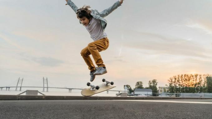 Dreng, der hopper på skateboard på gaden. Sjov barneskøjter, der praktiserer ollie på skateboard ved solnedgang.